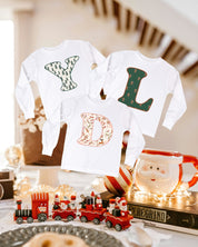 Child long sleeve in white with Christmas patterned initials on front, shown on flat lay – Little Mama Shirt Shop