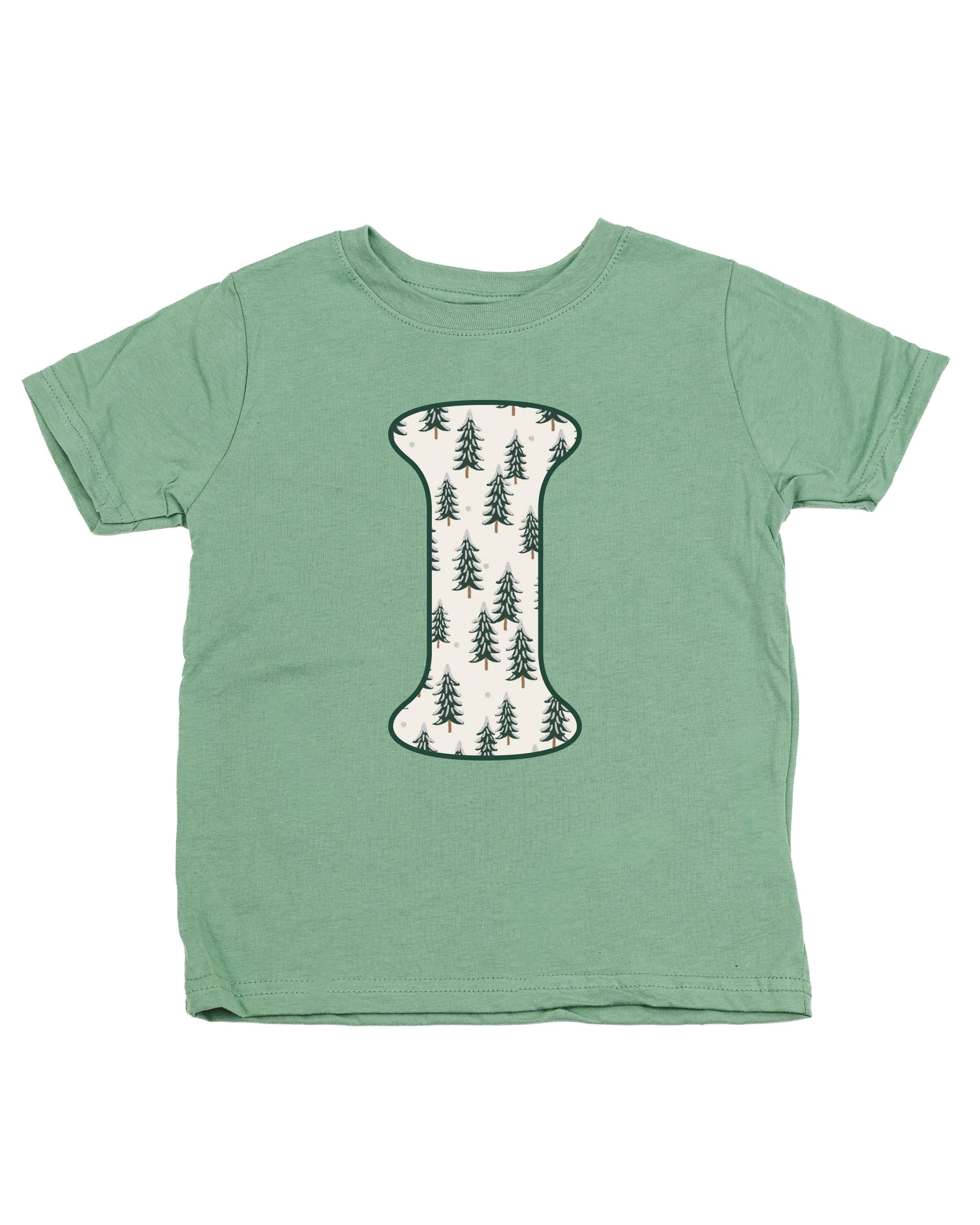 Child tee in sage with Christmas pattern trees with initial I on front, shown on flat lay – Little Mama Shirt Shop