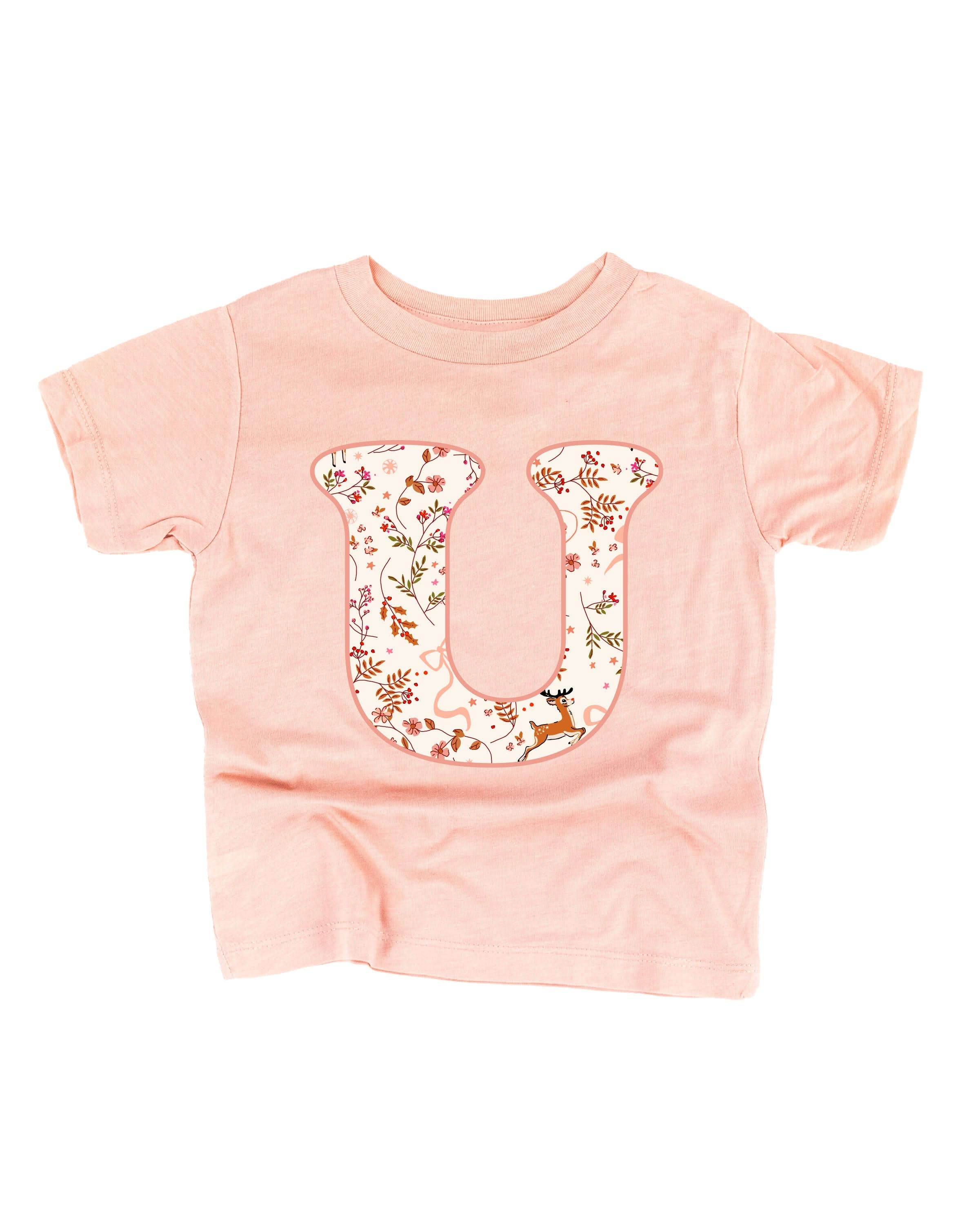 Child tee in blush with Christmas pattern reindeer with initial U on front, shown on flat lay – Little Mama Shirt Shop