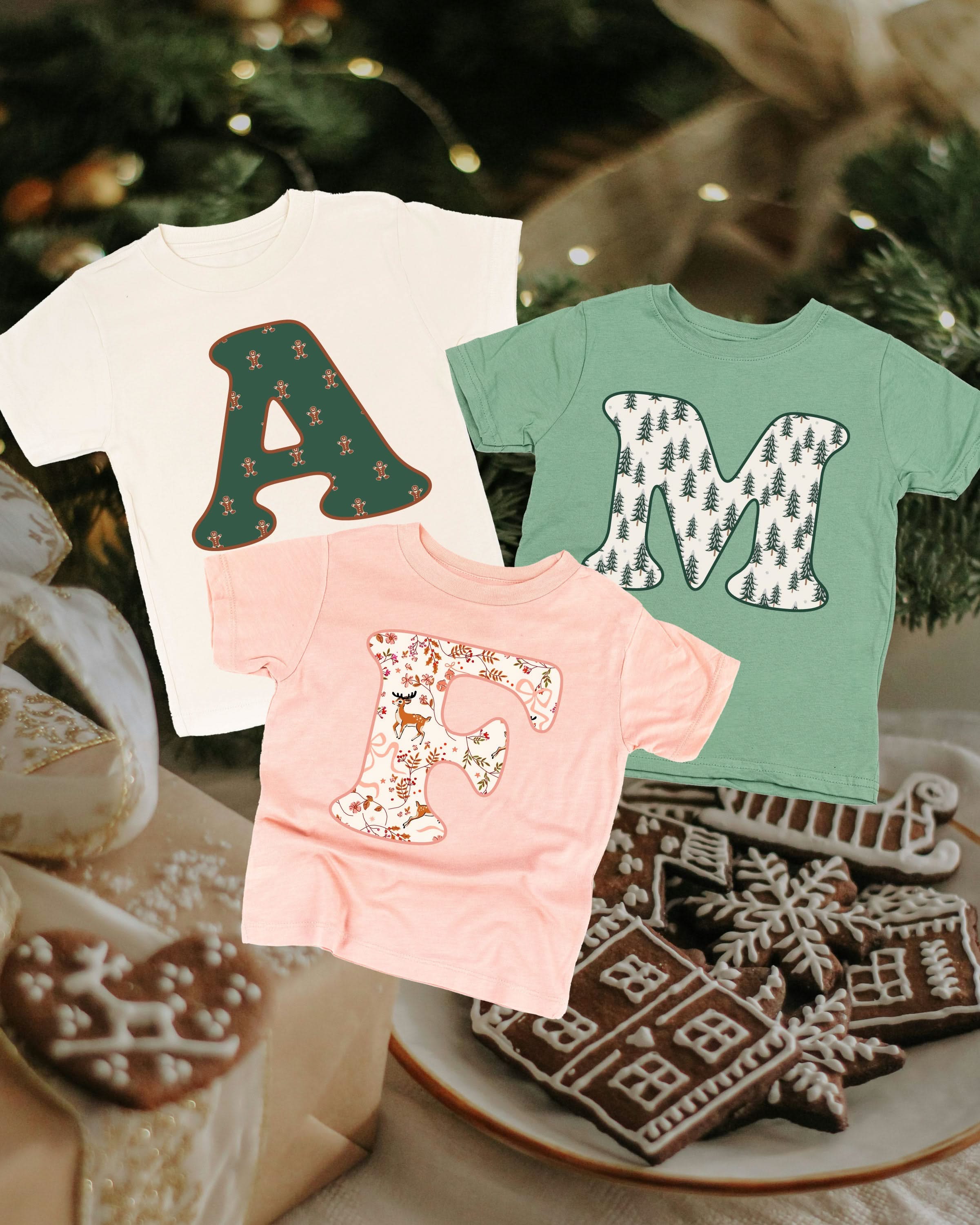 Child tees in natural, sage, and blush with Christmas patterned initials on front, shown on flat lay – Little Mama Shirt Shop