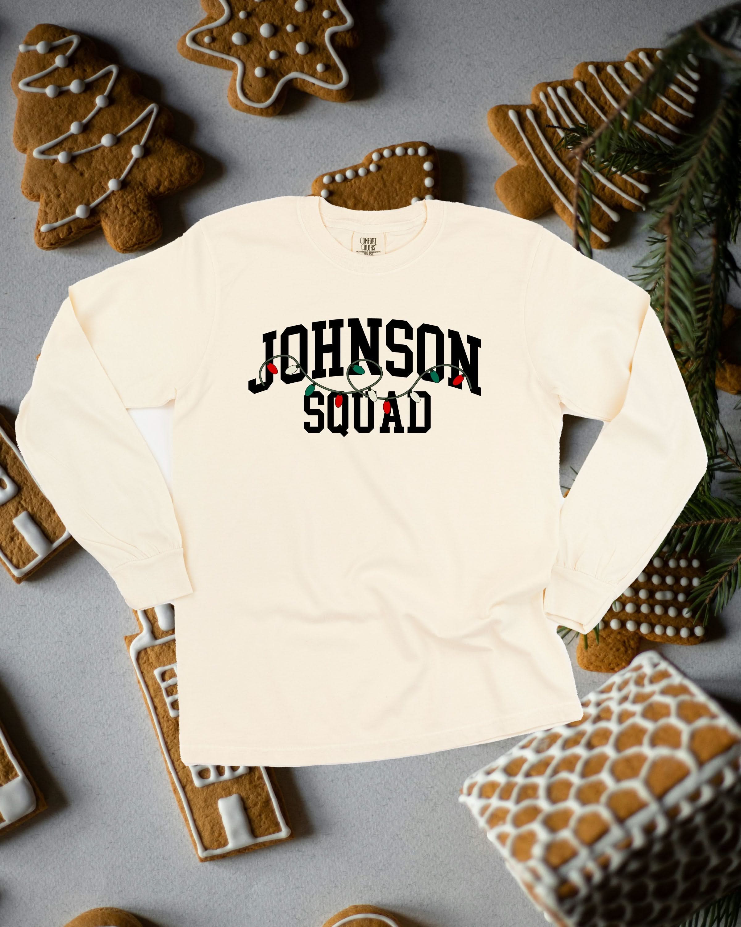 Long sleeve comfort colors tee in ivory with personalized last name printed on front with Christmas lights under, shown on flat lay – Little Mama Shirt Shop