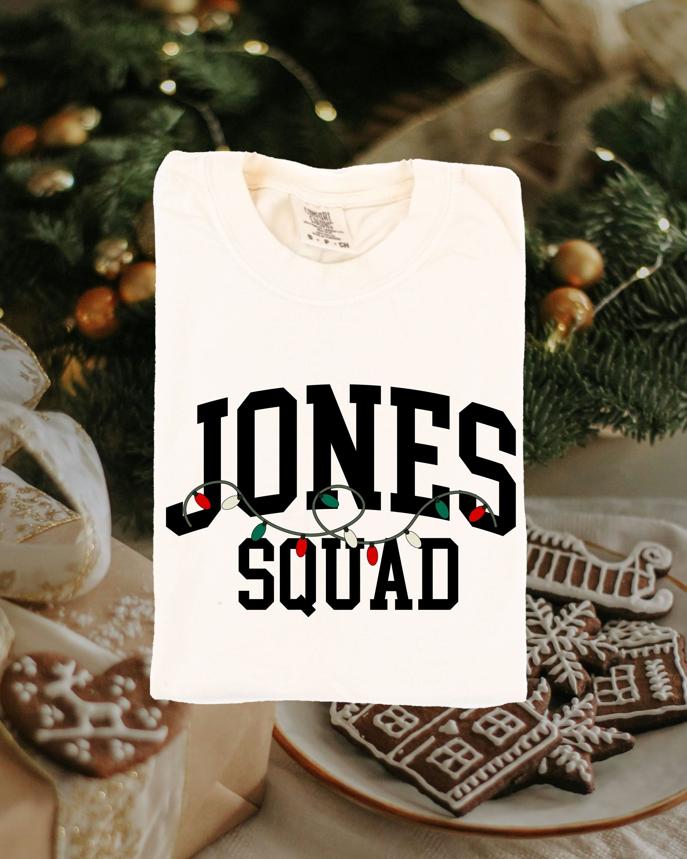 Comfort colors tee in ivory with personalized last name printed on front with Christmas lights under, shown on flat lay – Little Mama Shirt Shop