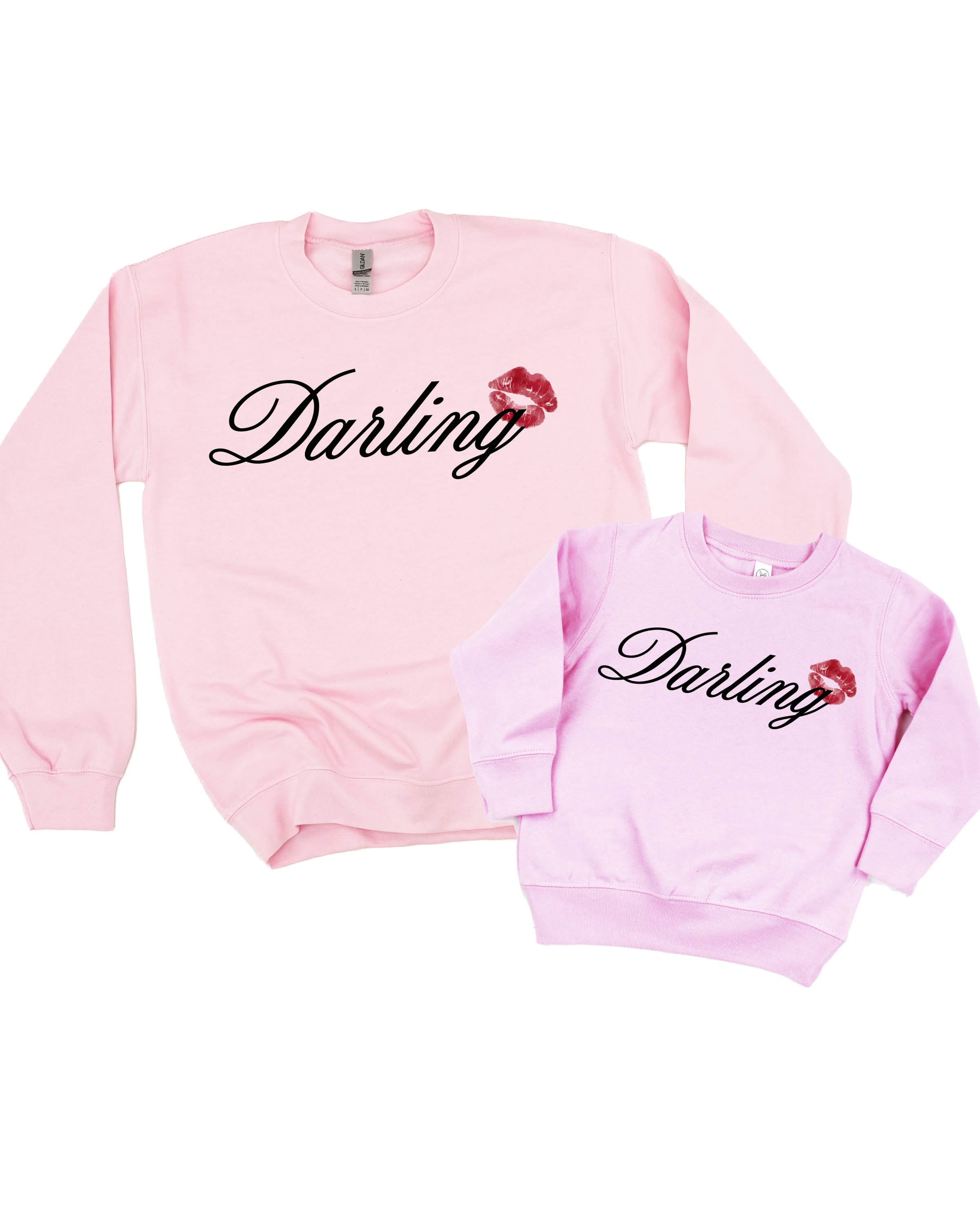 Adult and child pink sweaters with "Darling" script and lipstick kiss design, shown on flat lay  – Little Mama Shirt Shop