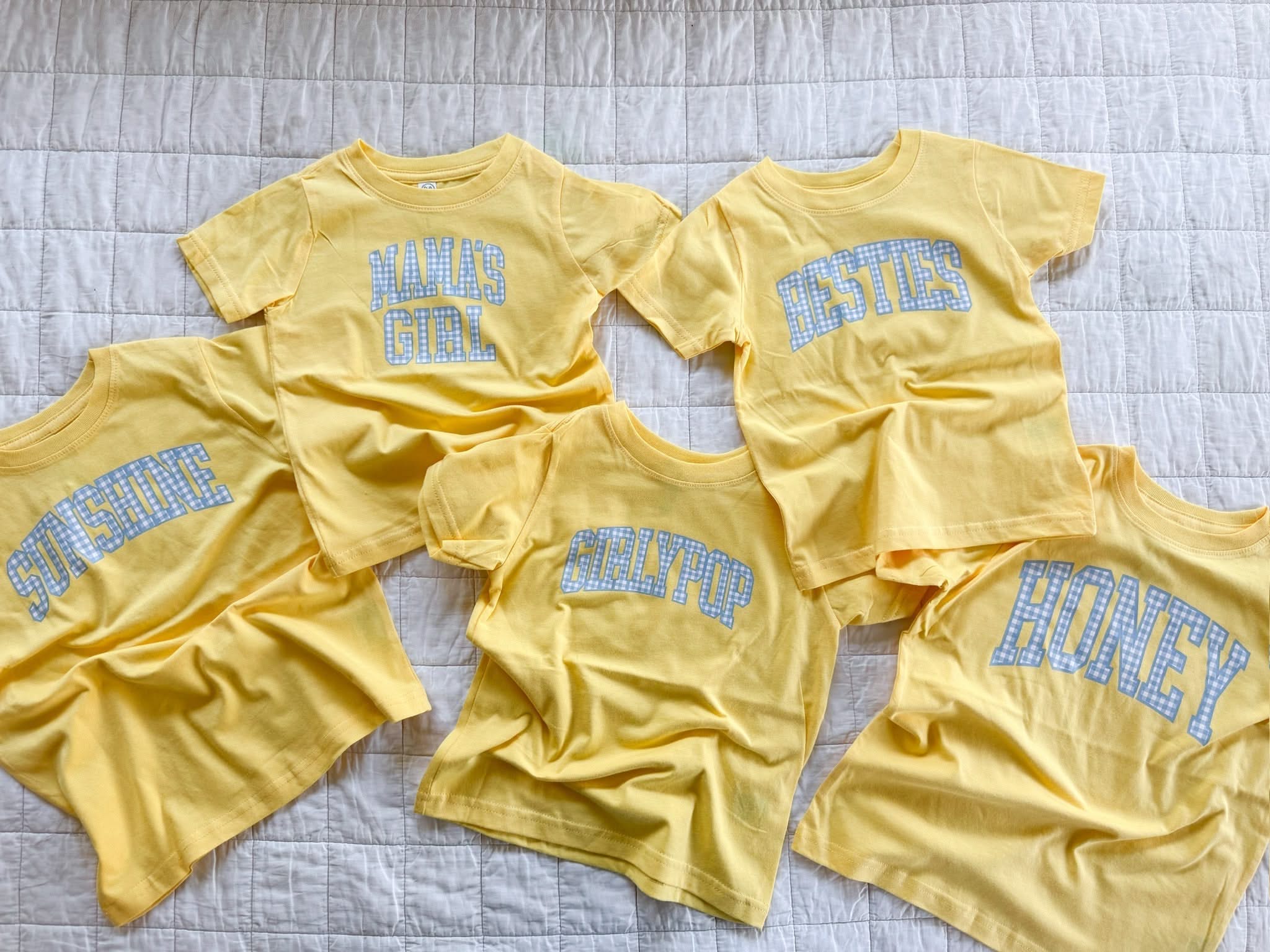 Collection of girls butter yellow gingham shirts with different phrase options spread out