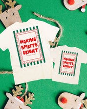Adult ivory and child natural tees with 'making spirits bright' graphic on back, shown on flat lay – Little Mama Shirt Shop