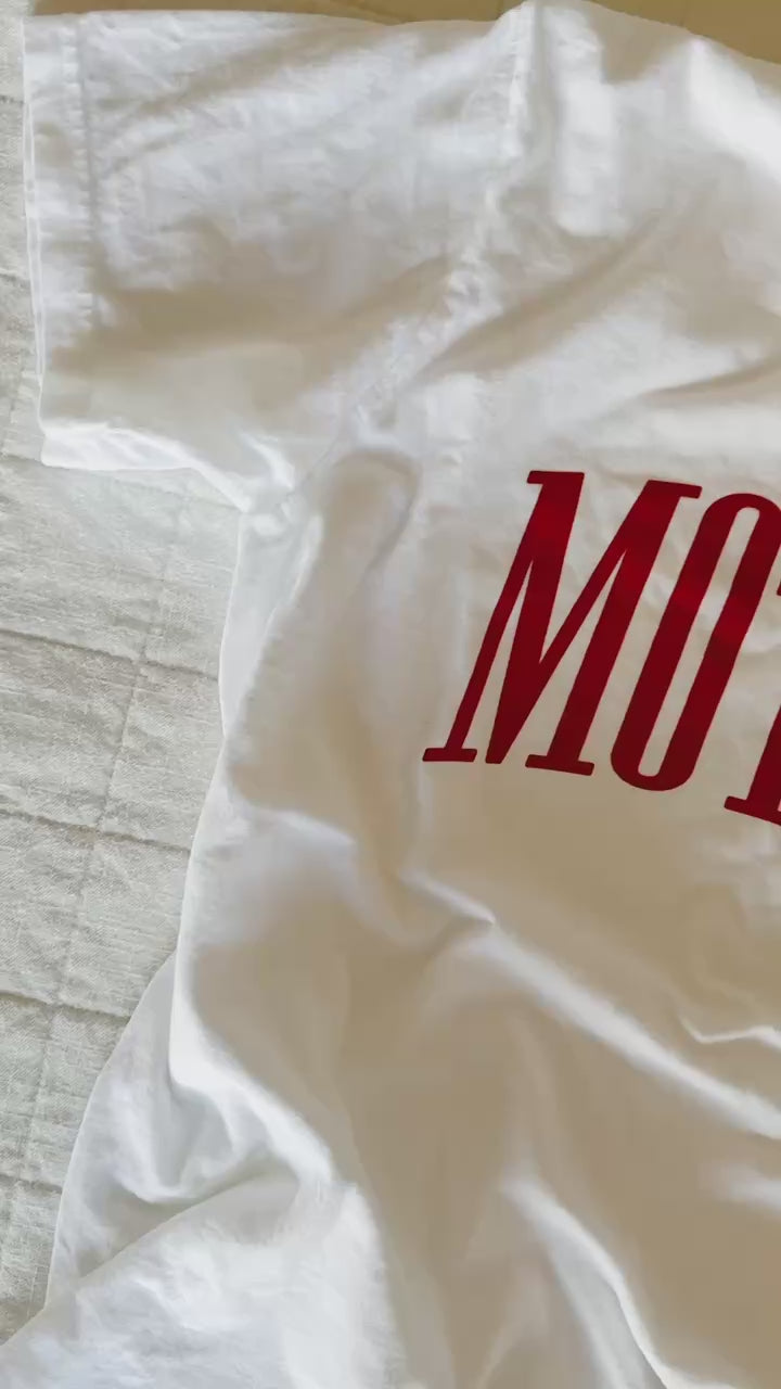 Video of white adult comfort colors tee with red 'mother' puff print across the front, seen on flat lay - Little Mama Shirt Shop
