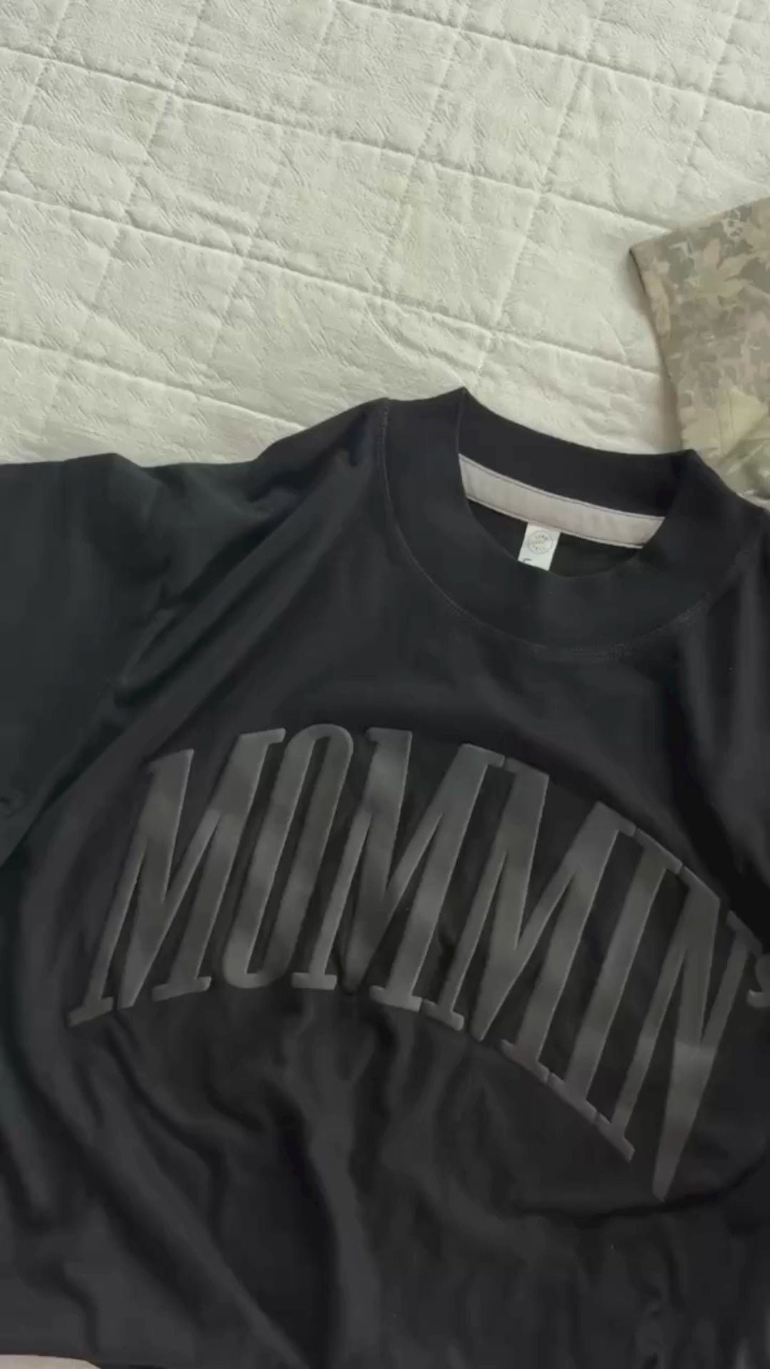 Video of adult boxy tee in black with 'mommin' printed on the front in puff print and camo tee with 'mother' printed on the front in puff print, seen on flat lay - Little Mama Shirt Shop