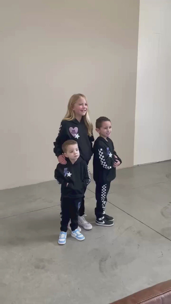 Video of child black sweater and joggers with checkers pattern on arm and leg, and Purple Heart or blue lightning bolt with 'be you' in it flanked by a white star, seen on models - Little Mama Shirt Shop