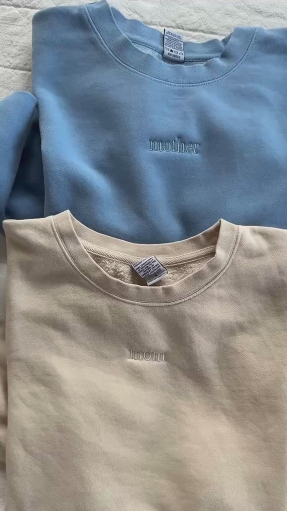 Video of adult crewneck in alpine, cream, blush, and light blue with mama, mom, or mother embroidered on the chest, seen on flat lay - Little Mama Shirt Shop