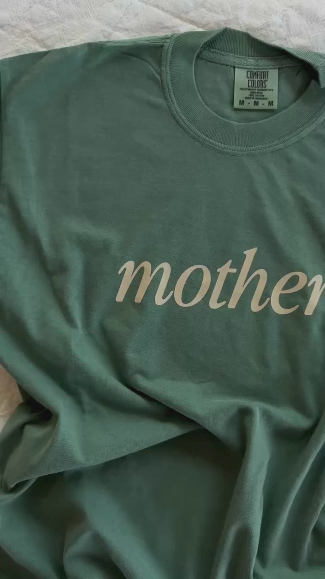 Video of adult tee in alpine with 'mother' printed on the front, seen on flat lay - Little Mama Shirt Shop