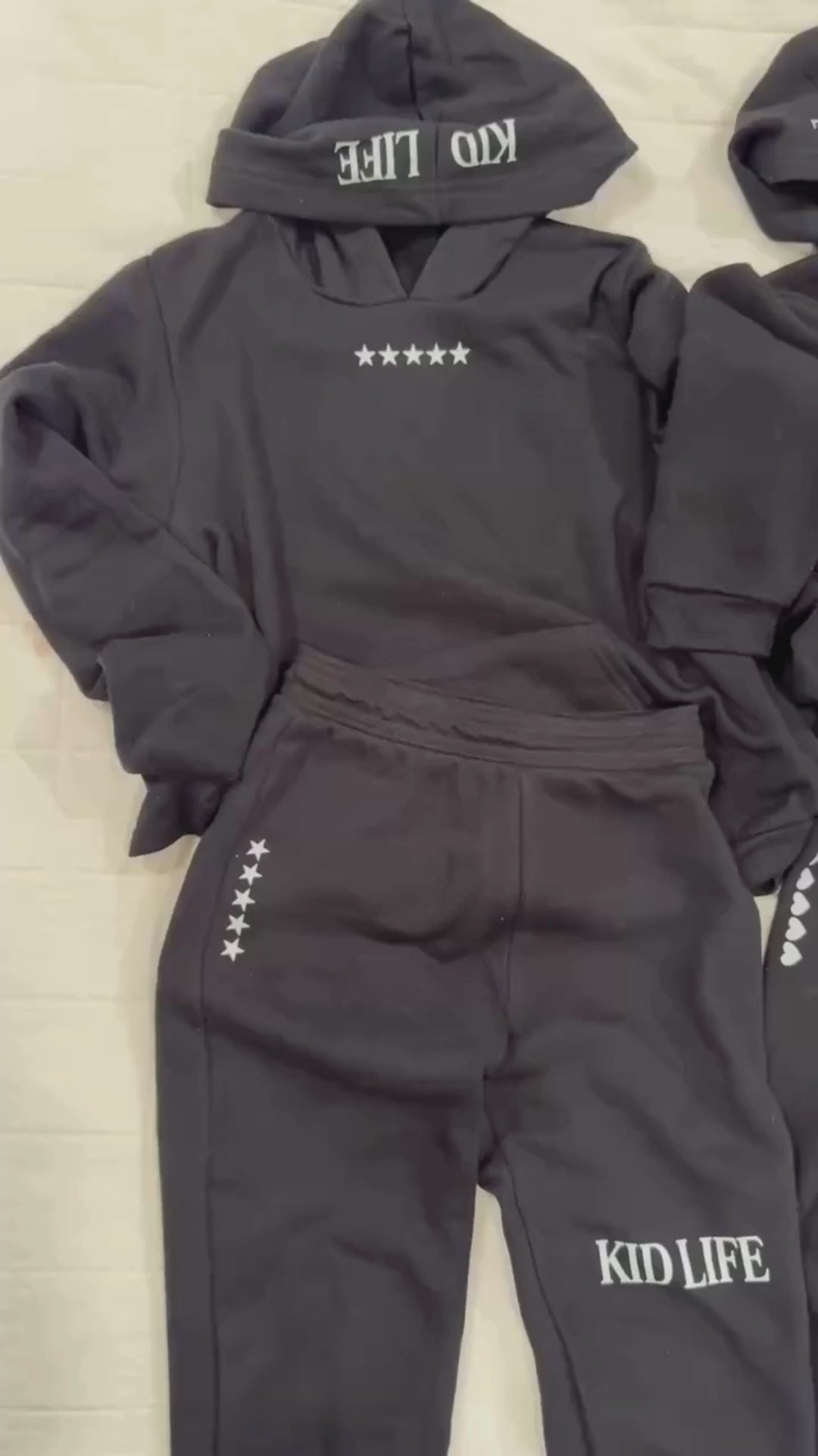 Video of hoodies in black with white 'Kid Life' graphic on hood and stars and hearts on chest seen on flat lay - Little Mama Shirt Shop