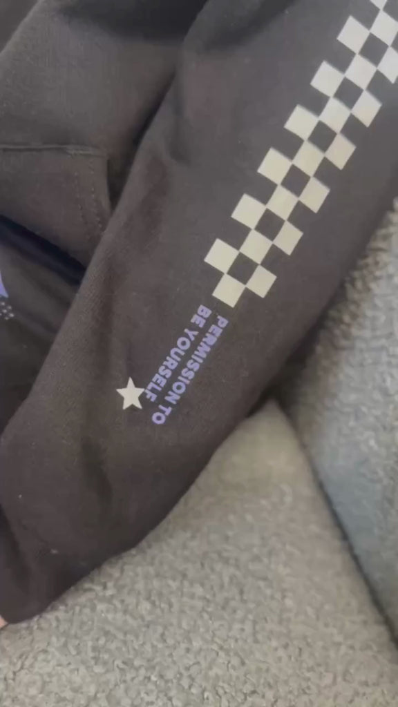 Video of child black sweater with checkers pattern on arm and blue lightning bolt with 'be you' in it flanked by a white star, seen on flat lay - Little Mama Shirt Shop