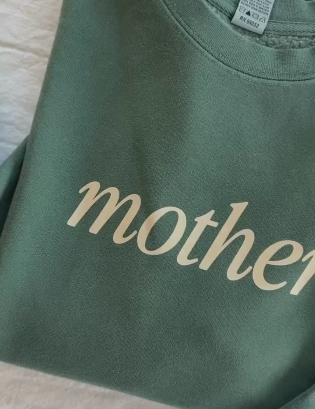 Video of adult pigment crewneck in alpine with 'mother' printed on the front and 'house full, hands full, heart full' printed on sleeve, seen on flat lay - Little Mama Shirt Shop