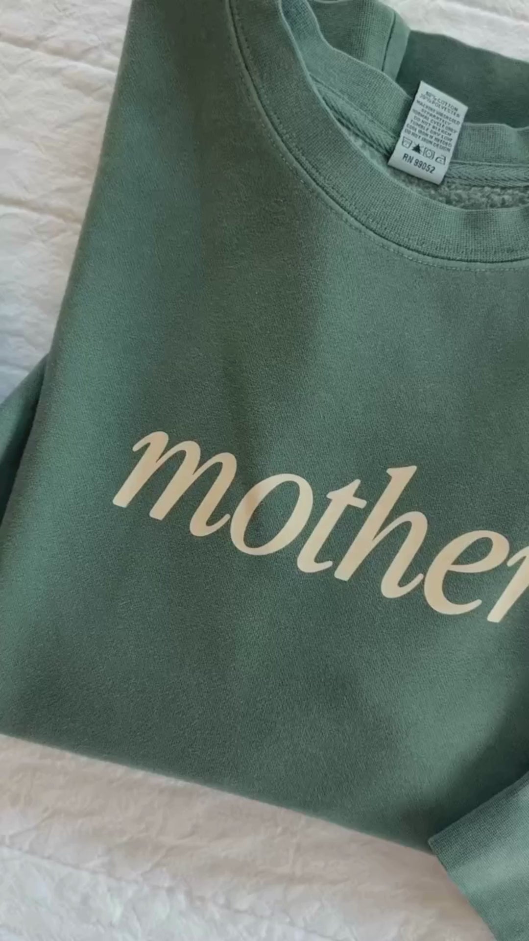 Video of adult pigment crewneck in alpine with 'mother' printed on the front and 'house full, hands full, heart full' printed on sleeve, seen on flat lay - Little Mama Shirt Shop
