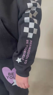 Video of child black sweater and joggers with checkers pattern on arm and leg, and Purple Heart with 'be you' in it flanked by a white star, seen on model - Little Mama Shirt Shop