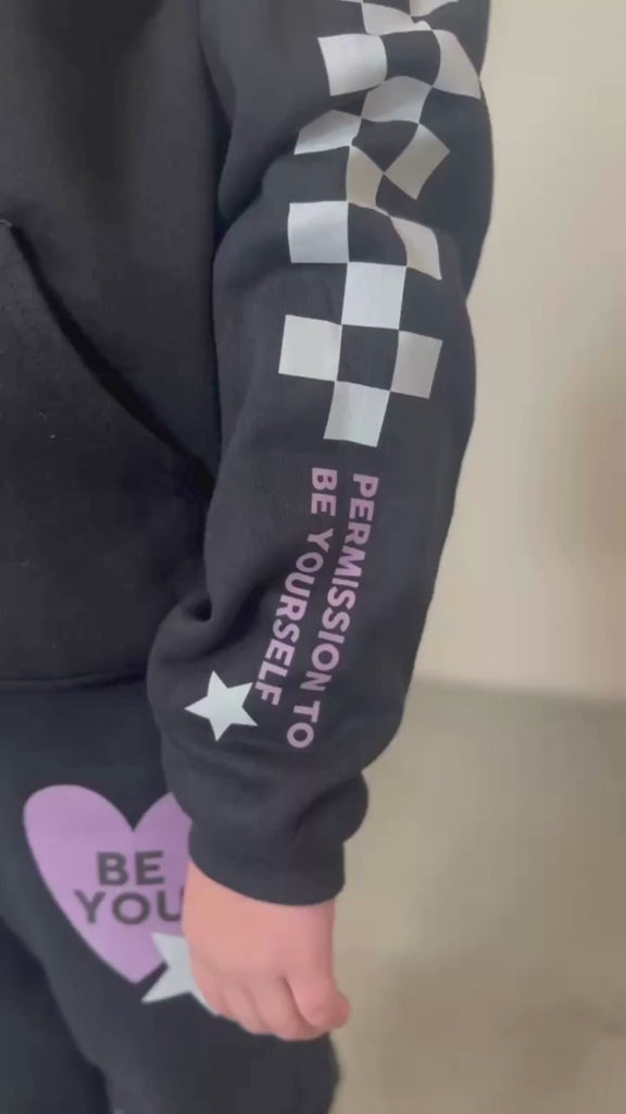 Video of child black sweater and joggers with checkers pattern on arm and leg, and Purple Heart with 'be you' in it flanked by a white star, seen on model - Little Mama Shirt Shop
