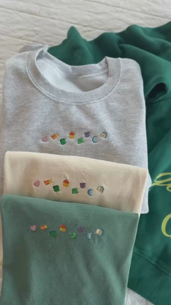 Video of gray sweater, green tee, and ivory tee with lucky charms design and  Green adult quarter zip with 'these are the good old days' printed on the back, seen on flat lay - Little Mama Shirt Shop