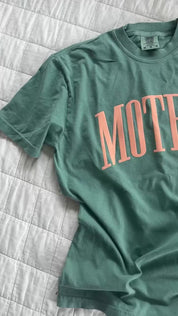 Video of light green adult comfort colors tee with coral 'mother' puff print across the front, seen on flat lay - Little Mama Shirt Shop