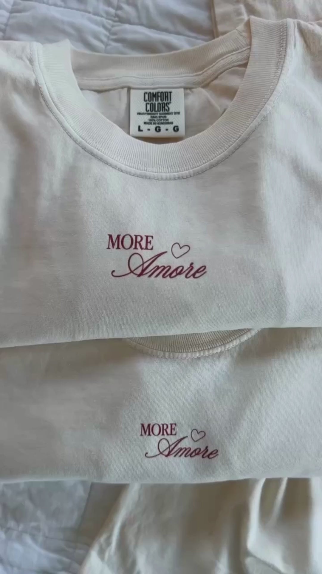 Video of Adult tee in ivory with "More Amore" print on front and Valentines collage design on back, shown on flat lay – Little Mama Shirt Shop