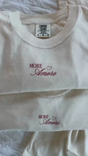 Video of Adult tee in ivory with "More Amore" print on front and Valentines collage design on back, shown on flat lay – Little Mama Shirt Shop
