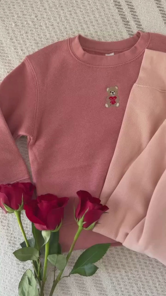 Video of child mauvelous and adult pink sweaters with valentine's teddy Embroidery on front, shown on flat lay  – Little Mama Shirt Shop