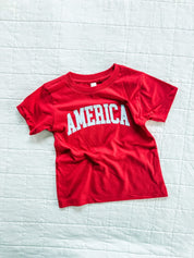 Red AMERICA shirt for kids with gingham lettering, bright and playful for summer celebrations